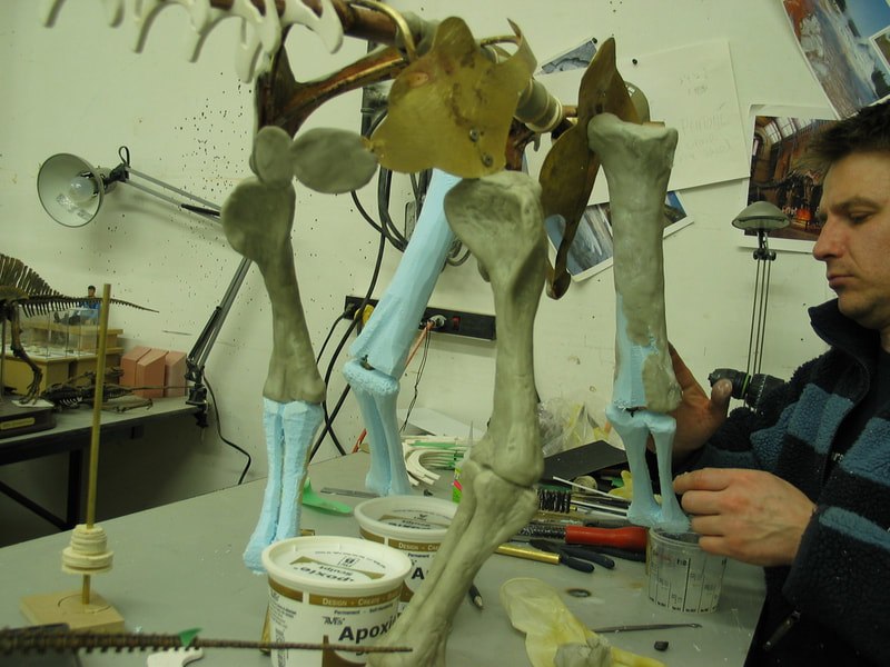 An artist sculpting a dinosaur skeleton for a miniature movie set.